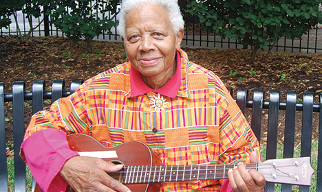 Ella Jenkins seated on a bench playing the guitar