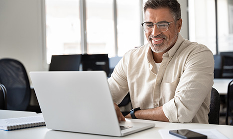 an older man seated and smiling at a laptop