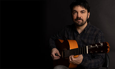 headshot of Goran Ivanovic sitting while holding a guitar on his lap