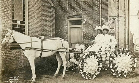old black-and-white photo of two Black women started in a horse-drawn carriage covered in flowers