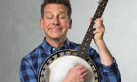 Jim Gill posing with a banjo in hand. His eyes are closed.