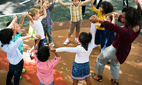 group of kindergarteners and an adult holding hands and standing in a circle outdoors