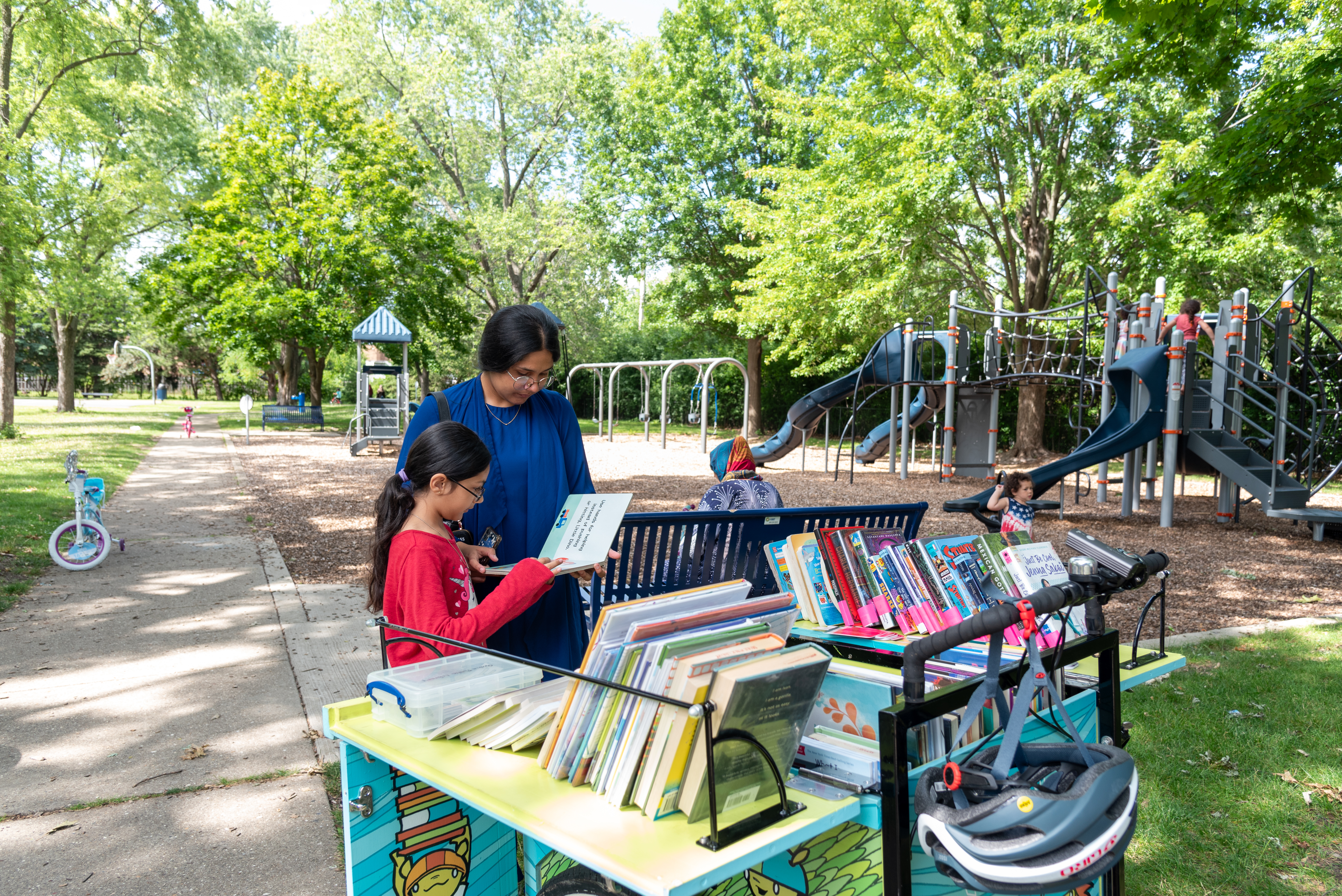 An adult and a child are browsing books on the book bike