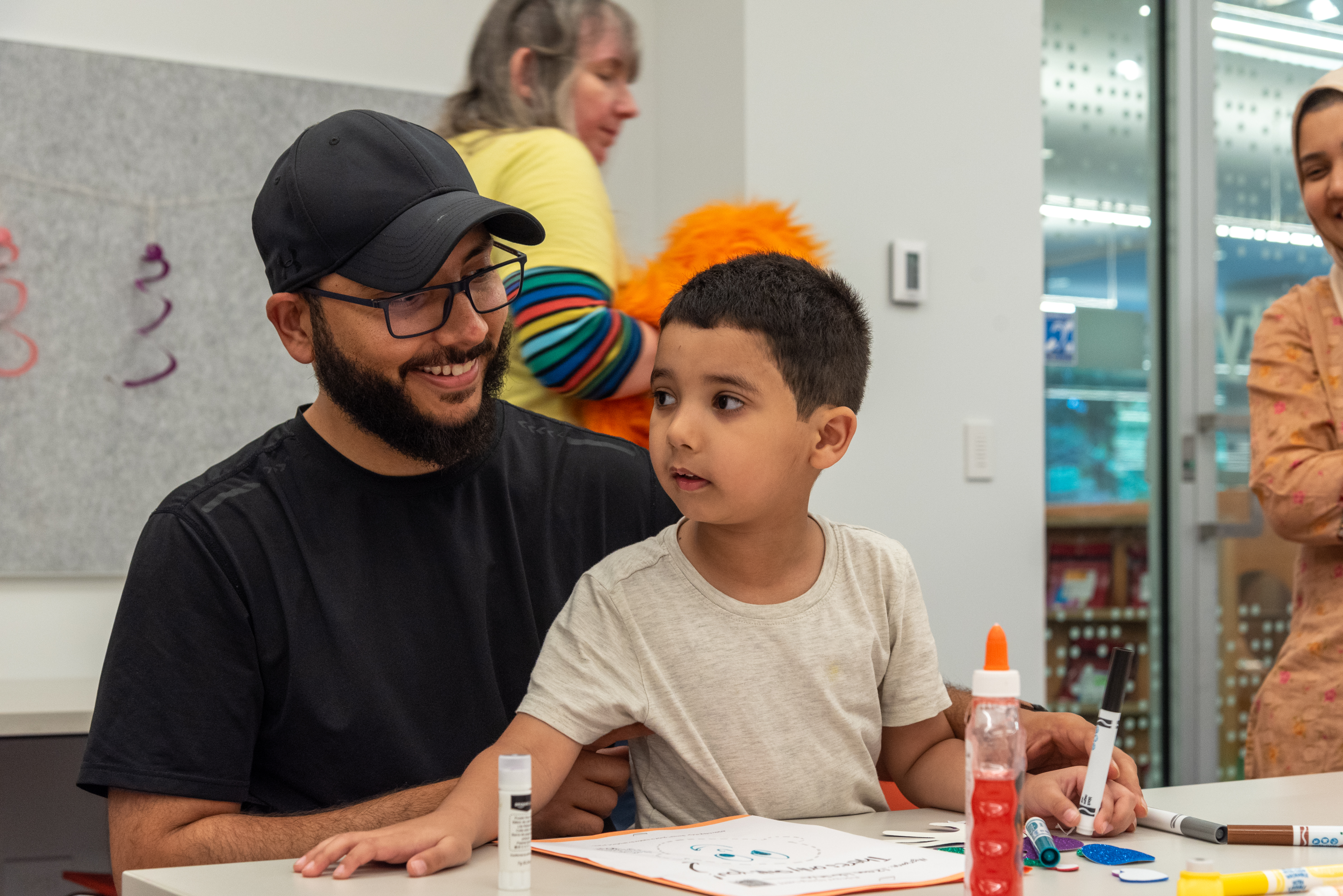 a young child is sitting with a man while surrounded by art supplies on a table in the Activity Room. 