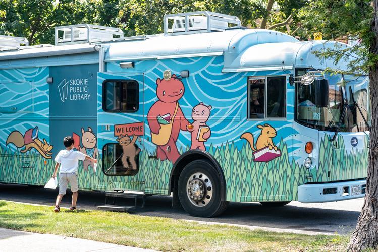 A boy holding a bag opens the door to the bright blue bookmobile bus A boy holding a bag opens the door to the bright blue bookmobile bus