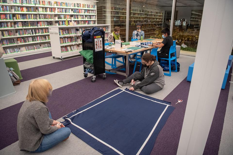 Teens and staff members spread out across a table and the floor while working on a textiles project in the Teen Room.