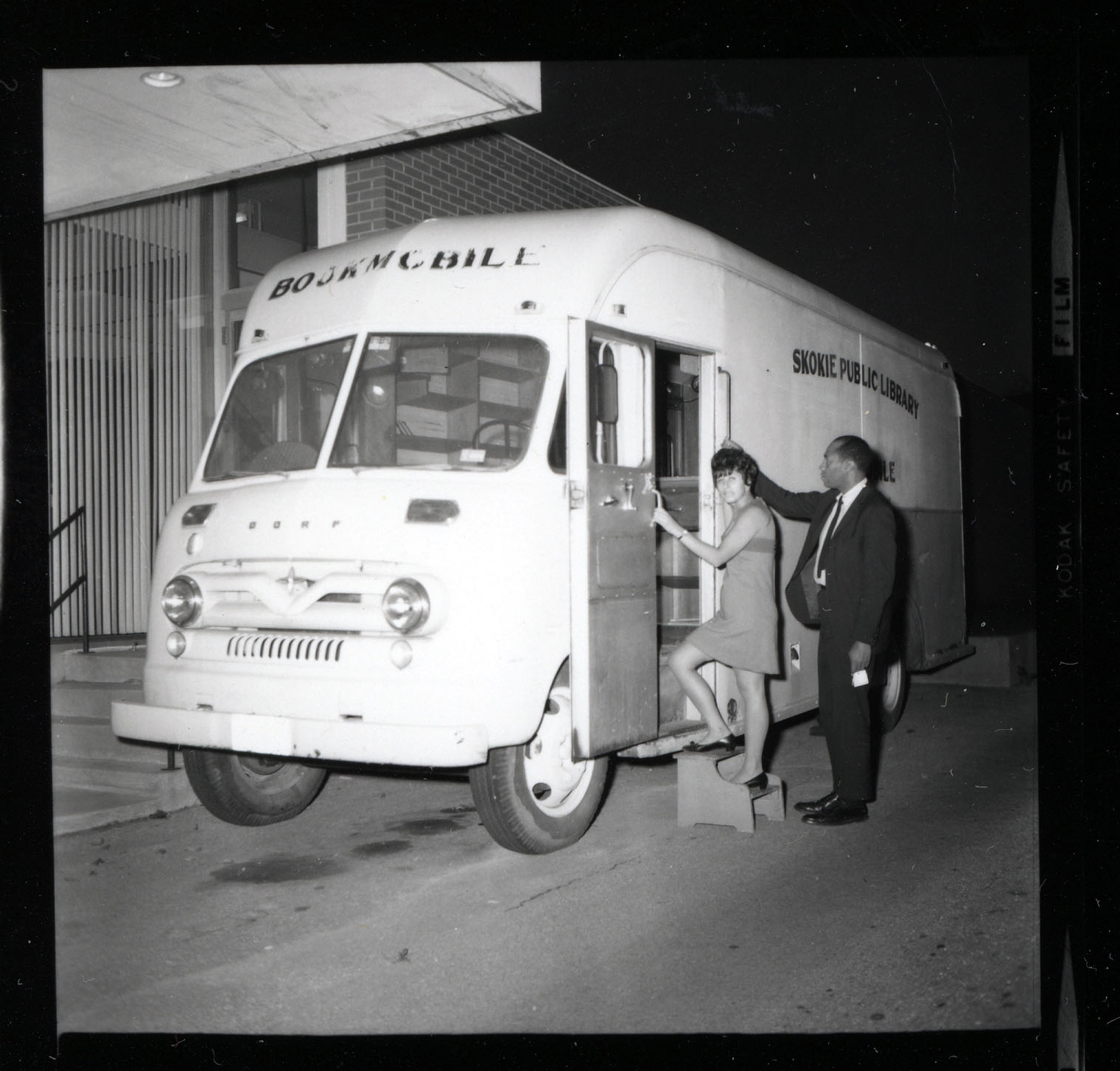 A black and white photograph of two people entering an early model of the Skokie Public Library bookmobile.