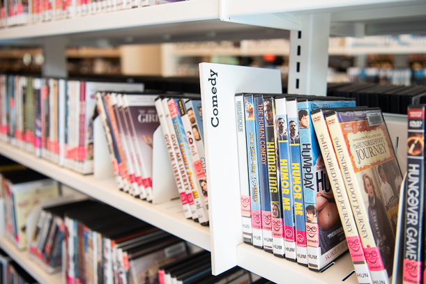 A photo of a white section divider reading "Comedy" that's placed on a shelf of DVDs and Blu-rays.