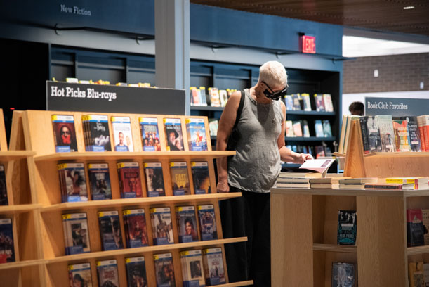 A library patron wearing a mask and flipping through a book on the Book Club Favorites display table on the first floor of the Skokie Public Library.