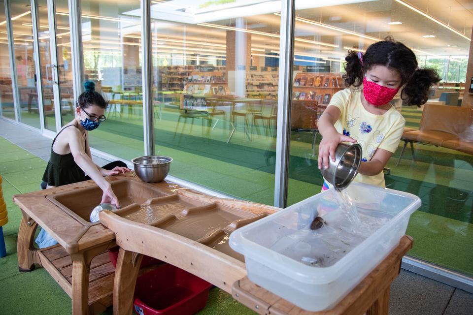 An adult and child play with the water table in the North Courtyard.