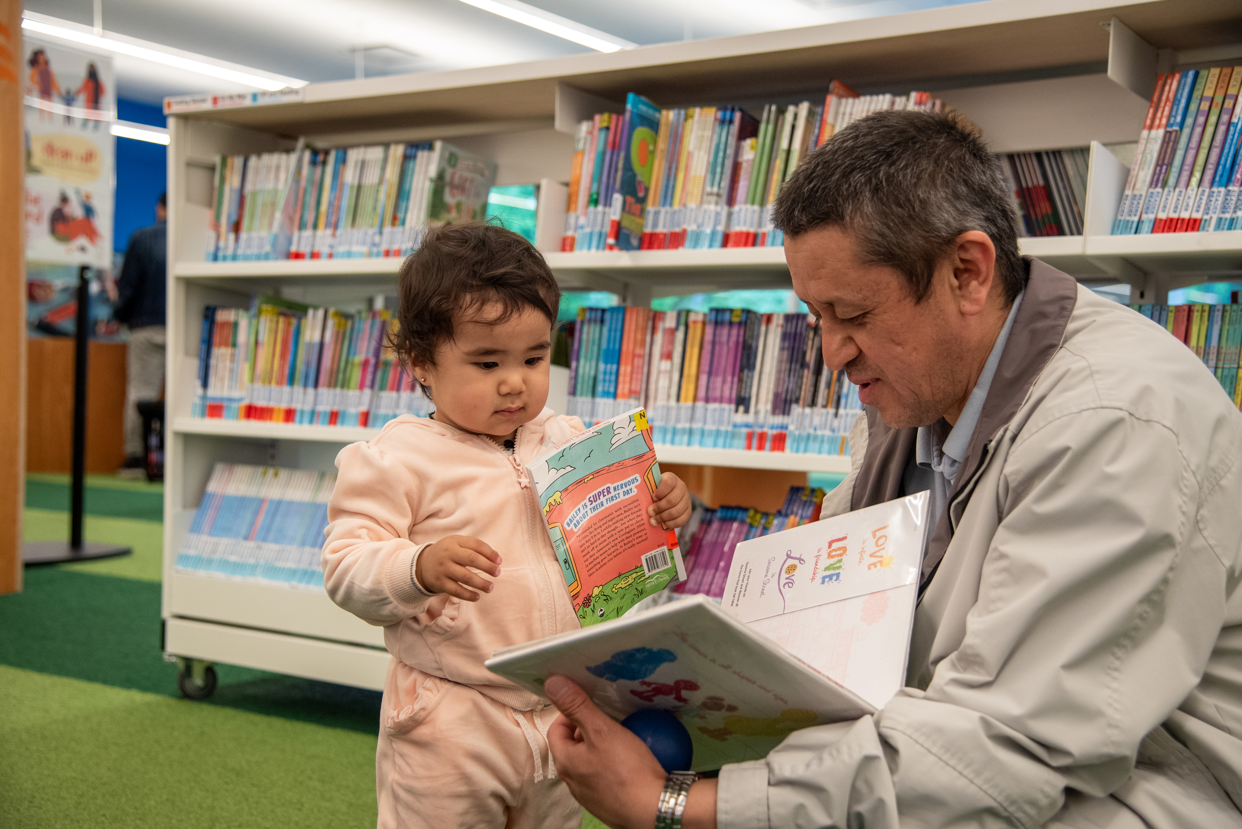 an older man is crouching to show a toddler the open pages of a picture book. 