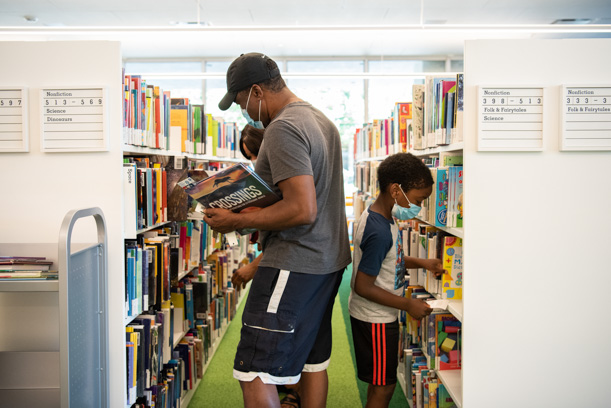 A family wearing masks and browsing shelves of books in the Kids area of the Skokie Public Library.