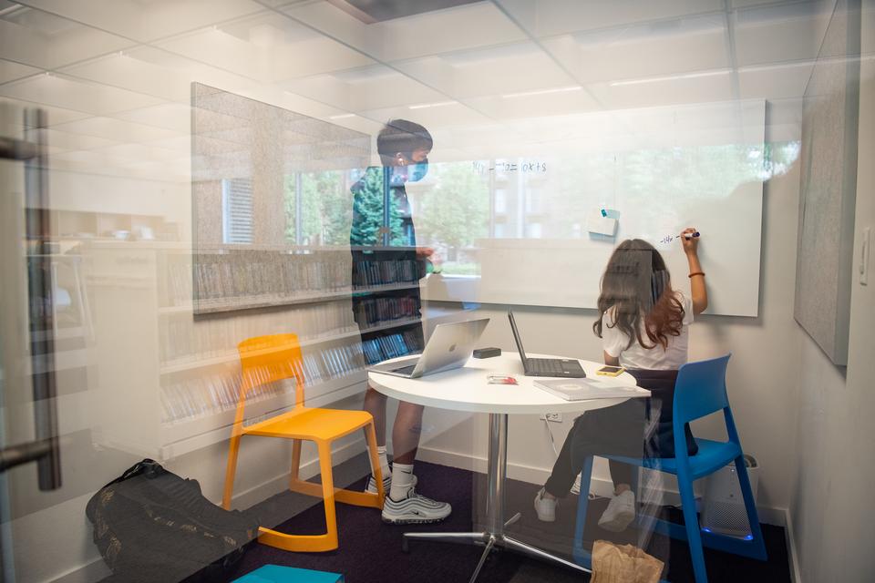 Two teens collaborate on a whiteboard inside one of the teen study rooms.