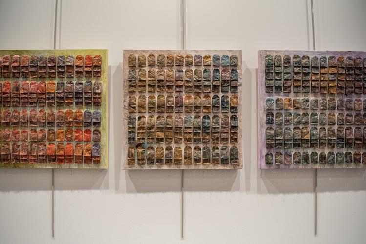 A photo of three textile works hanging on a wall. Each is a square comprised of smaller rectangles of highly textured threads in warm tones. A photo of three textile works hanging on a wall. Each is a square comprised of smaller rectangles of highly textured threads in warm tones.