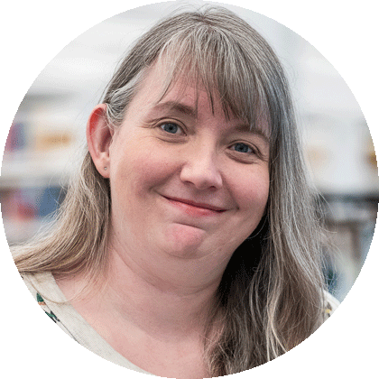 A woman with long grey hair and bangs smiles.