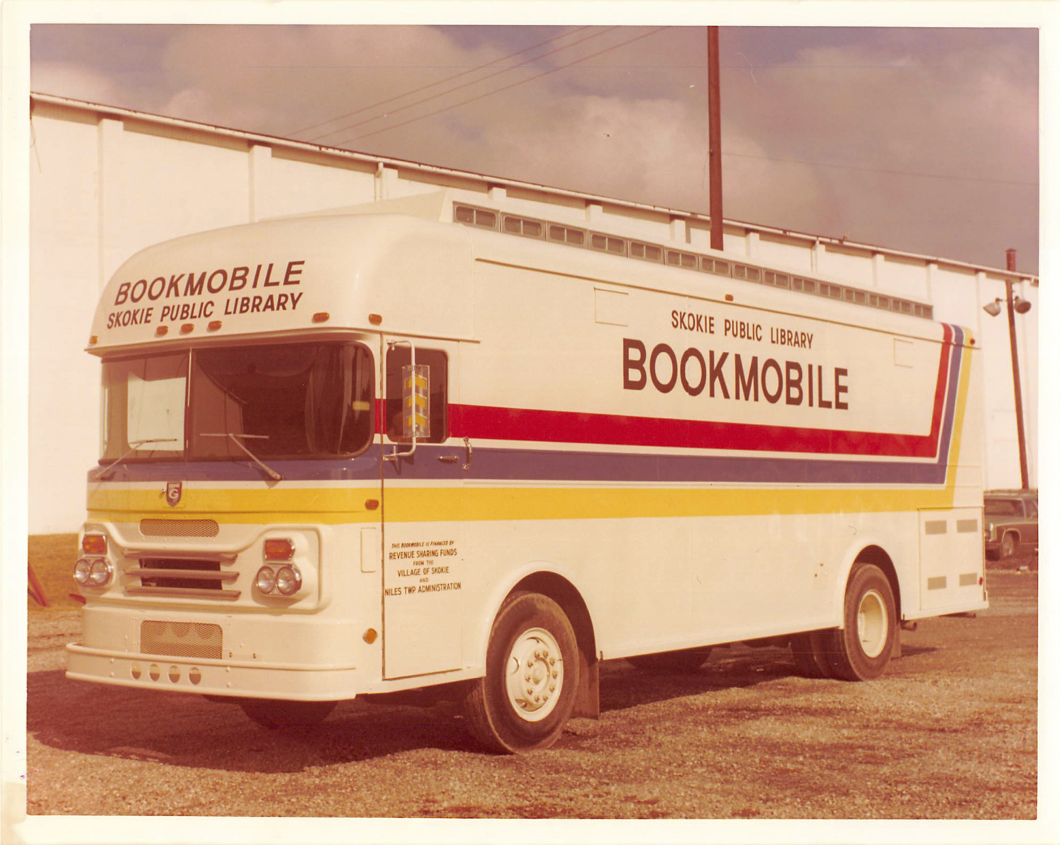 A yellowed photograph of a past model of the Skokie Public Library bookmobile, which is adorned with a red, blue, and yellow stripe down the side, above which reads "Bookmobile".